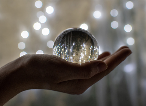Festive atmosphere in a crystal glass sphere. Reflections of holiday lights in a ball placed on her hands.