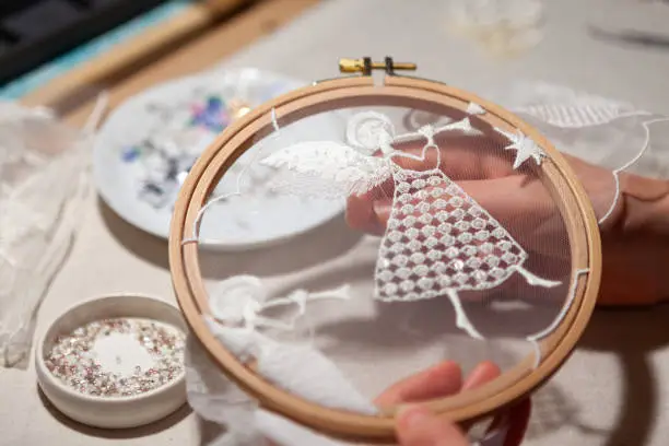 Workplace of an embroiderer with embroidery frames, angel embroidery, beads. The embroiderer's hands hold the embroidery hoop