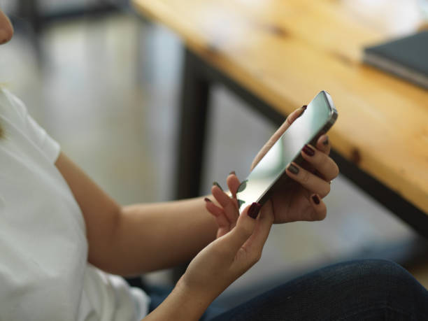 istock Female hand holding smartphone while sitting at workplace 1296950615