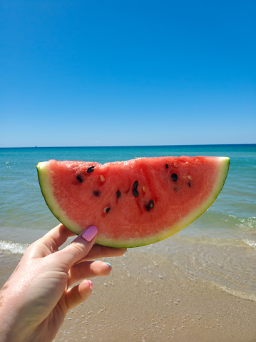 slice of watermelon in hand against the sea landscape on a Sunny day. the concept of summer vacation.