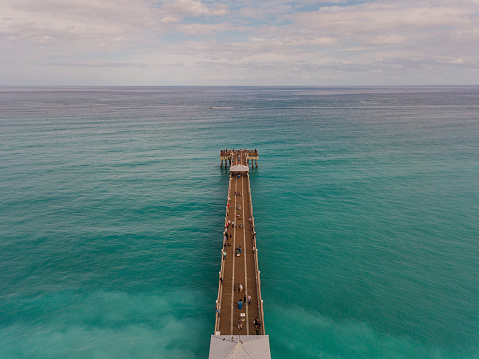 Aerial Views of the empty, blue Juno Beach seashore. Teal waves sweeping onto the clean shore. Blue skies with puffy clouds in the background.