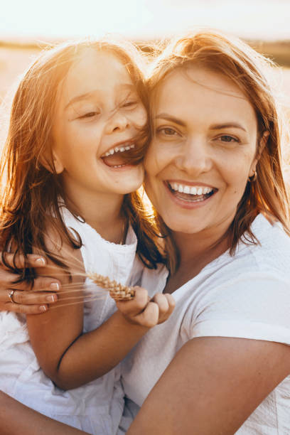 カメラで微笑む小麦の種で太陽の光の中でポーズをとる幸せな母親と彼女の娘 - mothers day 写真 ストックフォトと画像