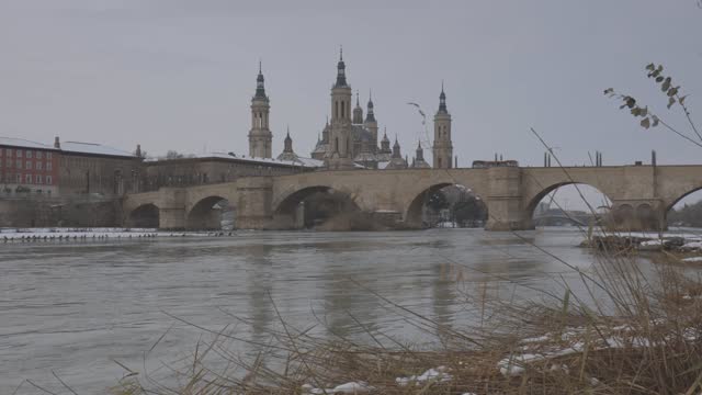 Panoramic view of Zaragoza, Basilica del Pilar and Ebro river. Remains of snow. Cormorants in the river. Canon log