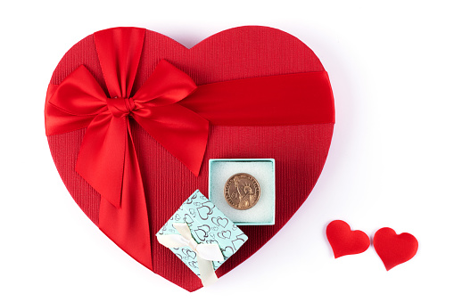 A 1 American dollar coin lies in a small open gift box on a large red cardboard human heart symbol on a white background