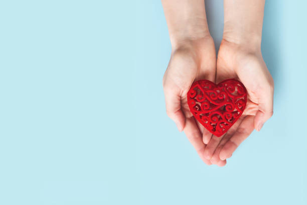 istock Womans hands holding red heart on blue background 1296971089