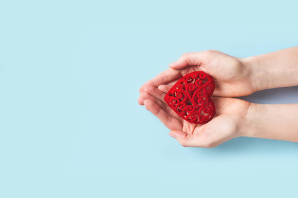 istock Womans hands holding red heart on blue background 1296971091