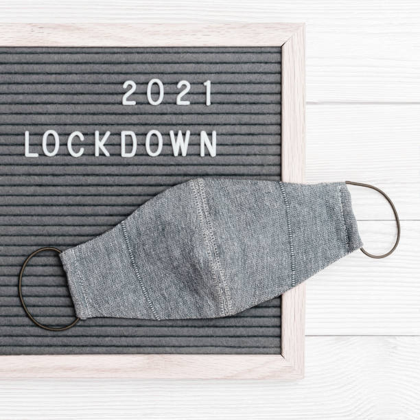 istock Grey colored Flatlay letter board with message text lockdown 2021 and protective face mask. Lock down loading concept. 1296971314
