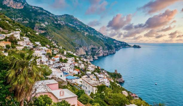 The charming Italian seaside town of Praiano, Italy, at sunset. Picturesque white and pastel houses perched above steep rocky cliffs with magnificent views of the Amalfi coast as fluffy clouds fill the sunset sky. praiano photos stock pictures, royalty-free photos & images