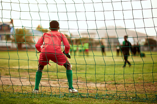 Rearview shot of a young boy standing as the goalkeeper while playing soccer on a sports field