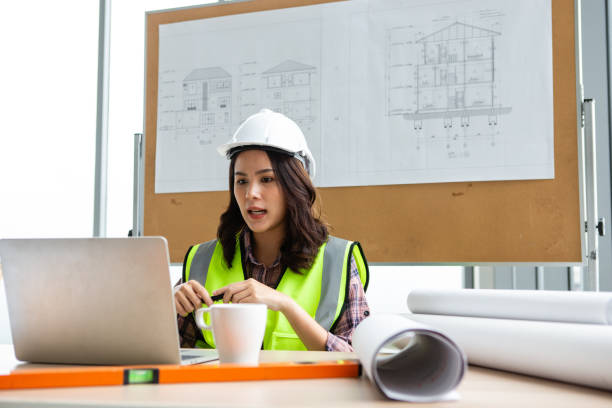engineer or architect with protective workwear using laptop for video call or selfie in front of modern business buildings and construction site