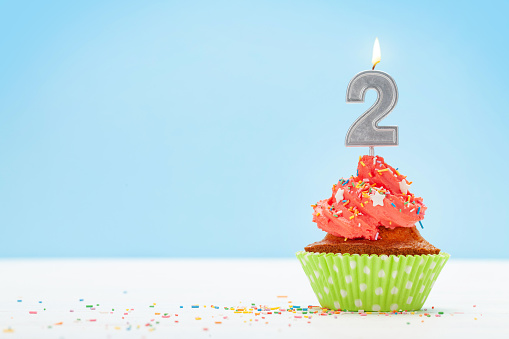 Birthday cupcake with number two burning candle over blue background with copy space for your greetings