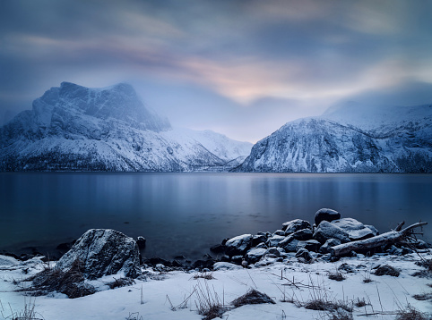 View on Norwegian sea and snowcapped mountain range during winter blue hour in Steinfjord, Norway.