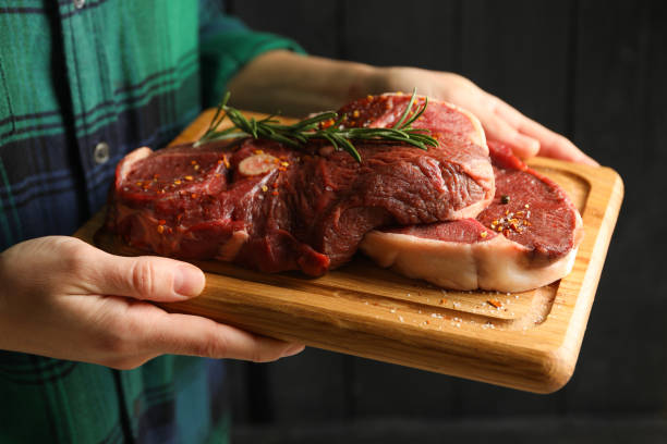 istock Woman hold board with raw steak meat, close up 1296985162