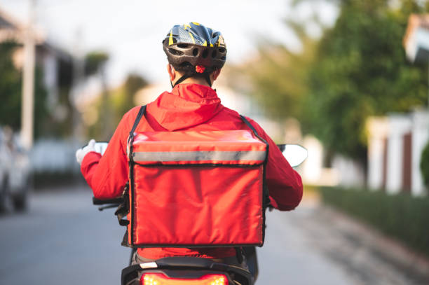 giovane che lavora per un servizio di consegna di cibo controllo con moto strada in città - corriere foto e immagini stock