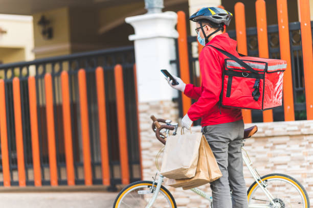 istock Delivery man wearing face protective mask to avoid corona virus red uniform Cycling to deliver products to customers at home. 1296986374