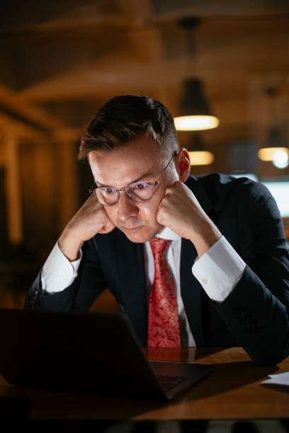 istock Tired man sitting at office desk working on laptop computer 1296987661