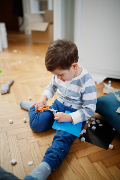 istock Toddler sitting on messy floor and cutting decorative paper 1296988070