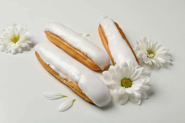 Delicious eclairs with custard and chamomiles on white background