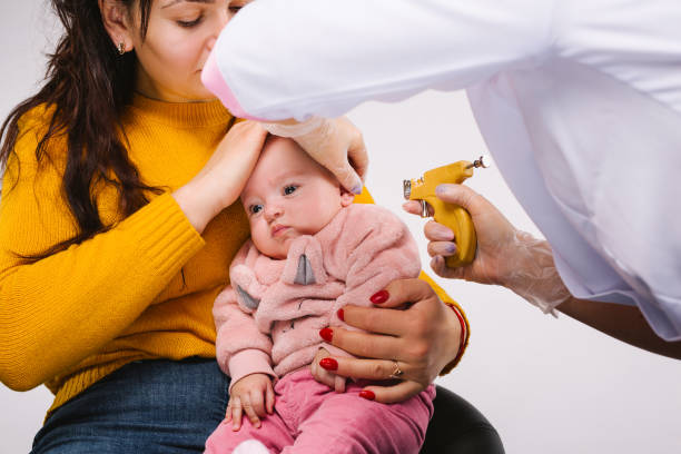 Enlarged photo. The doctor's hands are making holes in the ears with a pistol for a little baby. Enlarged photo. The doctor's hands are making holes in the ears with a pistol for a little baby. High quality photo baby gun stock pictures, royalty-free photos & images