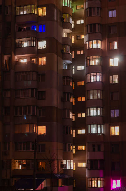 Noise, blur, defocus, soft focus, City apartments at night. Front view of high-rise building with windows of apartments in which light is burning.