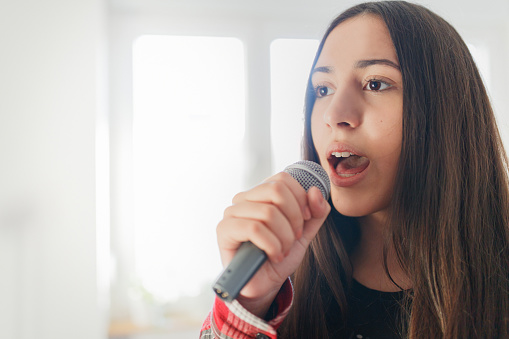 Close-up of teenage girl singing on wireless microphone at home, fighting boredom in COVID-19 pandemic lockdown