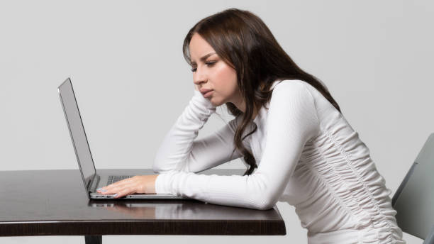 donna seduta a tavola, guardando e lavorando al laptop, isolata. posizione postura errata e compromessa, scoliosi dei difetti. - slouch hat foto e immagini stock