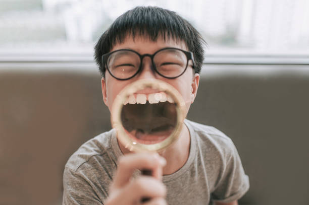 азиатский китайский подросток улыбка увеличить уход за зубами проведения увеличительное стекло на зубах глядя на камеру юмора - dentist asian ethnicity portrait male стоковые фото и изображения