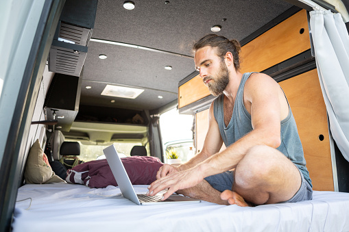 Young bearded man with a laptop inside his camper van.