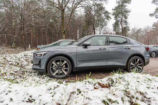 Polestar 2 all-electric 5-door fastback car side view in grey parked in a forest during a cold winter day with snow on the ground in Gelderland, The Netherlands. Polestar is the performance company and brand of Volvo Cars now focussed on producing electric and hybrid vehicles. The Polestar 2 is powered by two electric motors driving the front and rear wheels.