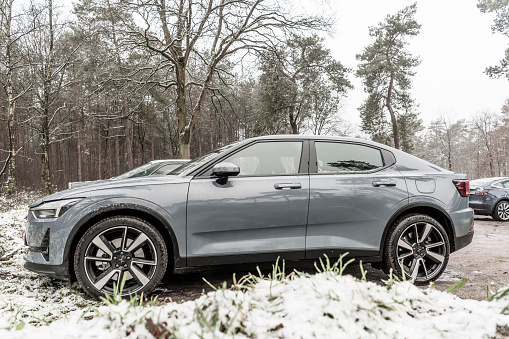 Polestar 2 all-electric 5-door fastback car side view in grey parked in a forest during a cold winter day with snow on the ground in Gelderland, The Netherlands. Polestar is the performance company and brand of Volvo Cars now focussed on producing electric and hybrid vehicles. The Polestar 2 is powered by two electric motors driving the front and rear wheels.