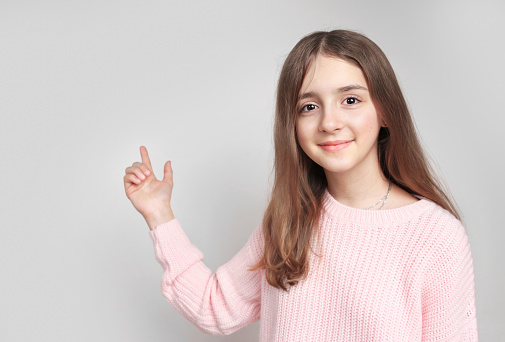 Beautiful person advertisement design blank.Young girl showing with finger empty space.Caucasian teen ager point grey background.Promotion backdrop.