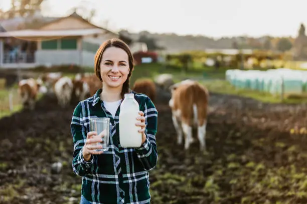 Portrait of young female farmer holding milk bottle with glass