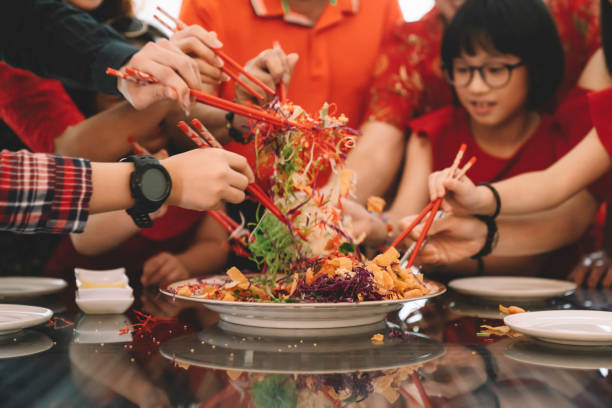 asiática familia china de varias generaciones celebrando la víspera de año nuevo chino con platos tradicionales de pescado crudo lau cantó yee durante la cena de reunión - cultura oriental fotografías e imágenes de stock