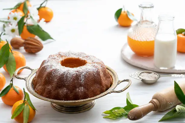 Bundt cake made of tangerine clementines baked homemade with ingredients on white wooden background