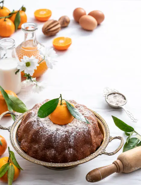 Bundt cake made of tangerine clementines baked homemade with ingredients on white wooden background