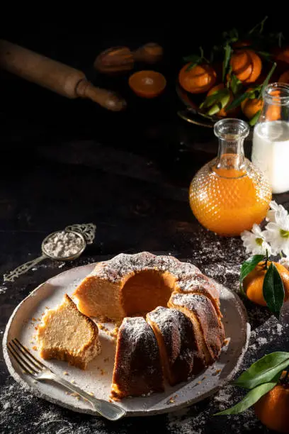 Bundt cake made of tangerine clementines baked homemade with ingredients on moody dark background