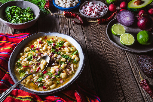 Pozole Mexican corn stew with meat, mote corn, radishes, coriander, lime and lettuce on wooden table