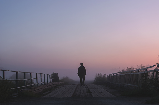 silhouette of a man walking on a wooden bridge in fog at dawn. Atmospheric rustic, rural  morning landscape