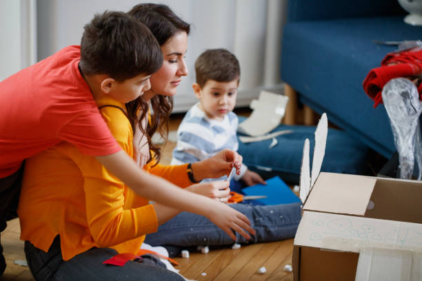 istock Mother ornating cardboard craft plane for her sons, older son leaning on her back 1297008784