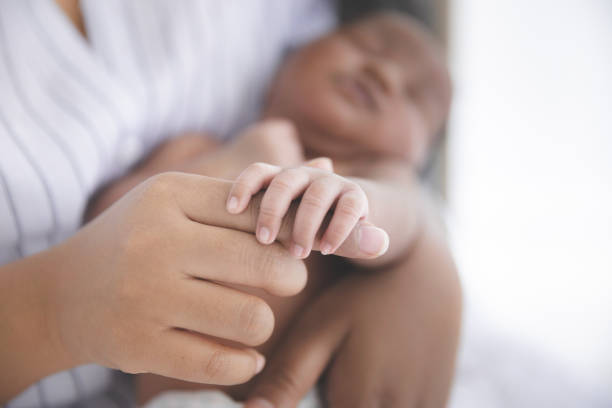 Mother holding hands newborn baby Close up Mother holding hands newborn baby in a room with a lot of sunlight, Newborn baby sleeping in the mother's embrace. Health care, love, relationship concept. biracial newborn stock pictures, royalty-free photos & images