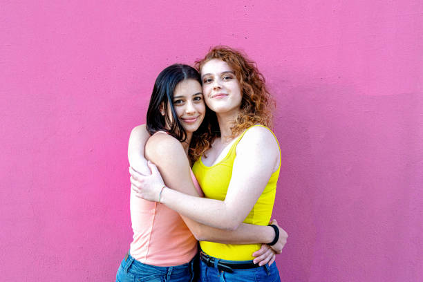 casal de jovens mulheres orgulhosamente abraçar, duas mulheres apaixonadas felizes e desinibidas, uma menina morena e uma menina vermelha abraçar em um abraço carinhoso, símbolo de orgulho gay e diversidade, direitos iguais lgbt - lesbian love sexual issues two people - fotografias e filmes do acervo