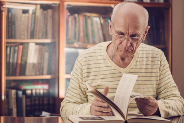 istock Mature grey haired professor sitting at table and leaf through pages of book 1297014372