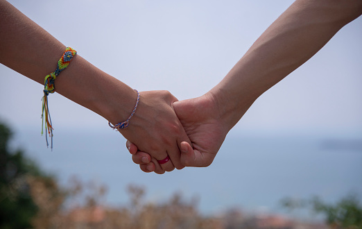 Two hands, male and female, holding each other tightly, on a blurred light background. On the female hand is a bright bracelet.