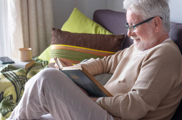 istock A white-haired elderly man relax at home reading a book on sofa. Bright light from the window. Retired seniors in lockdown due to coronavirus 1297016499