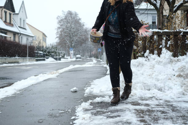 young millenial woman spreading salt on icy sidewalk in front of her house - people cold frozen unrecognizable person imagens e fotografias de stock