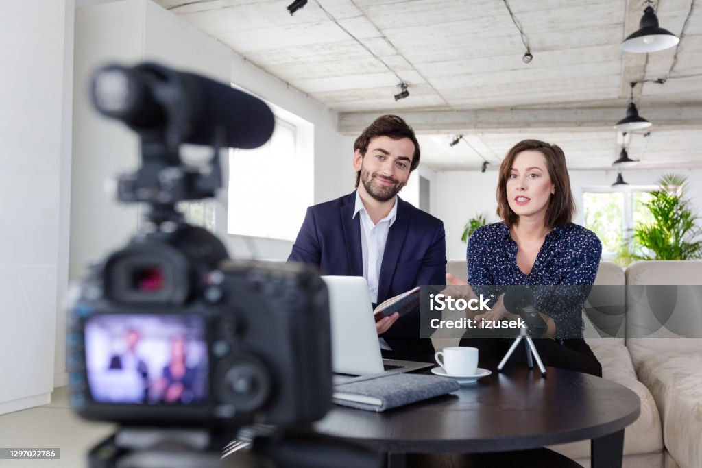 Coworkers making a video blog in the office Businessman and businesswoman making a video blog. Vloggers recording content on digital camera in the creative office, smiling at camera. Businesswoman Stock Photo