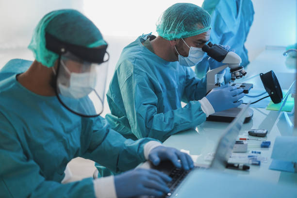 istock Medical workers in hazmat suit working with laptop computer and micoroscope inside laboratory hospital during coronavirus outbreak - Focus on center man face 1297025252