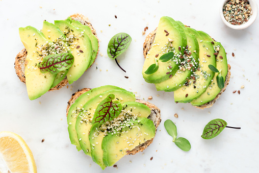 Avocado slices with seeds and micro greens on toasted bread on white background. Healthy vegan vegetarian avocado toasts, top view
