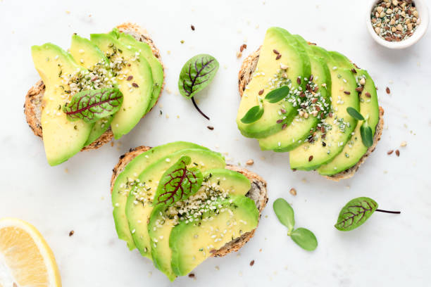 Avocado slices with seeds and micro greens on toasted bread Avocado slices with seeds and micro greens on toasted bread on white background. Healthy vegan vegetarian avocado toasts, top view avocado stock pictures, royalty-free photos & images
