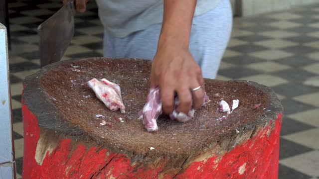A man is chopping with a cleaver fresh meat of a ram. Man cuts bones for frying